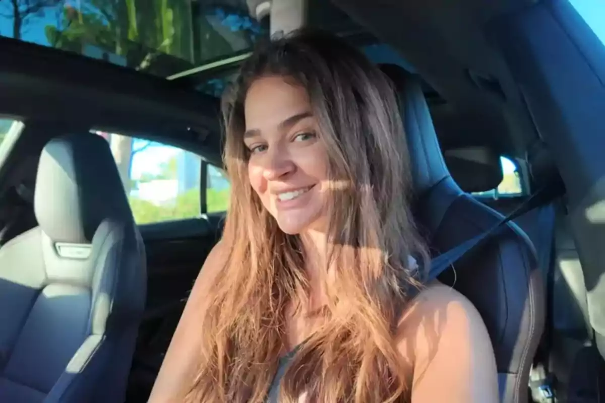 Mujer joven con cabello largo y suelto sonriendo mientras está sentada en el asiento del conductor de un automóvil