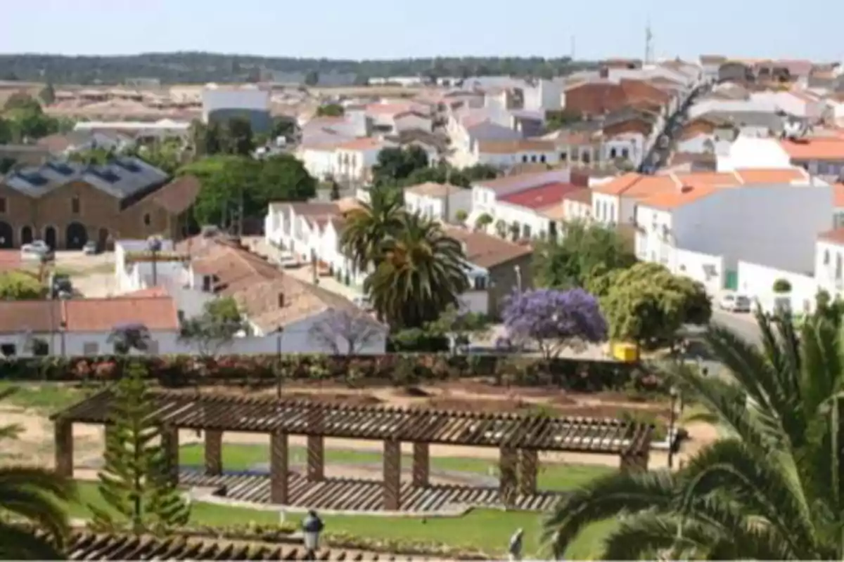 Vista panorámica de un pueblo con casas de techos rojos, árboles y un parque con pérgolas de madera en primer plano Vista panorámica de un pueblo con casas de techos rojos, árboles y un parque con pérgolas de madera en primer plano