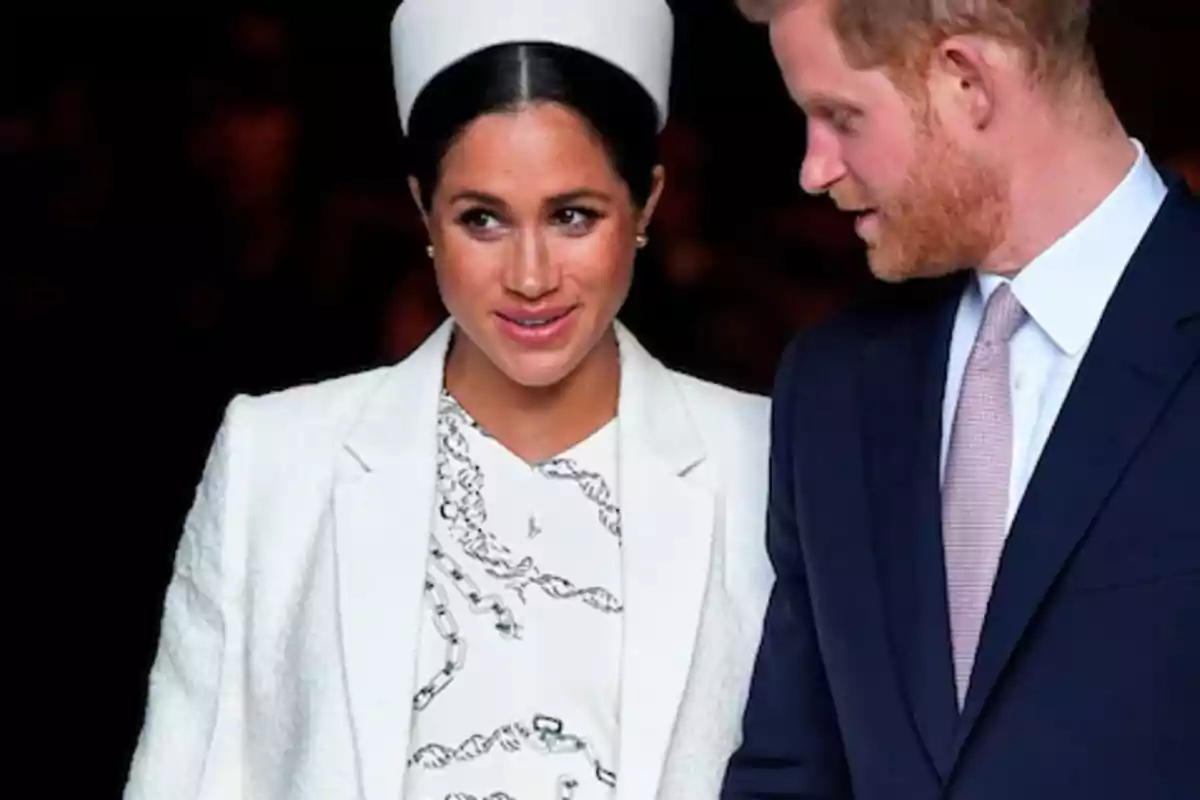 Una mujer con tocado blanco y abrigo claro junto a un hombre con traje oscuro y corbata clara Una mujer con tocado blanco y abrigo claro junto a un hombre con traje oscuro y corbata clara