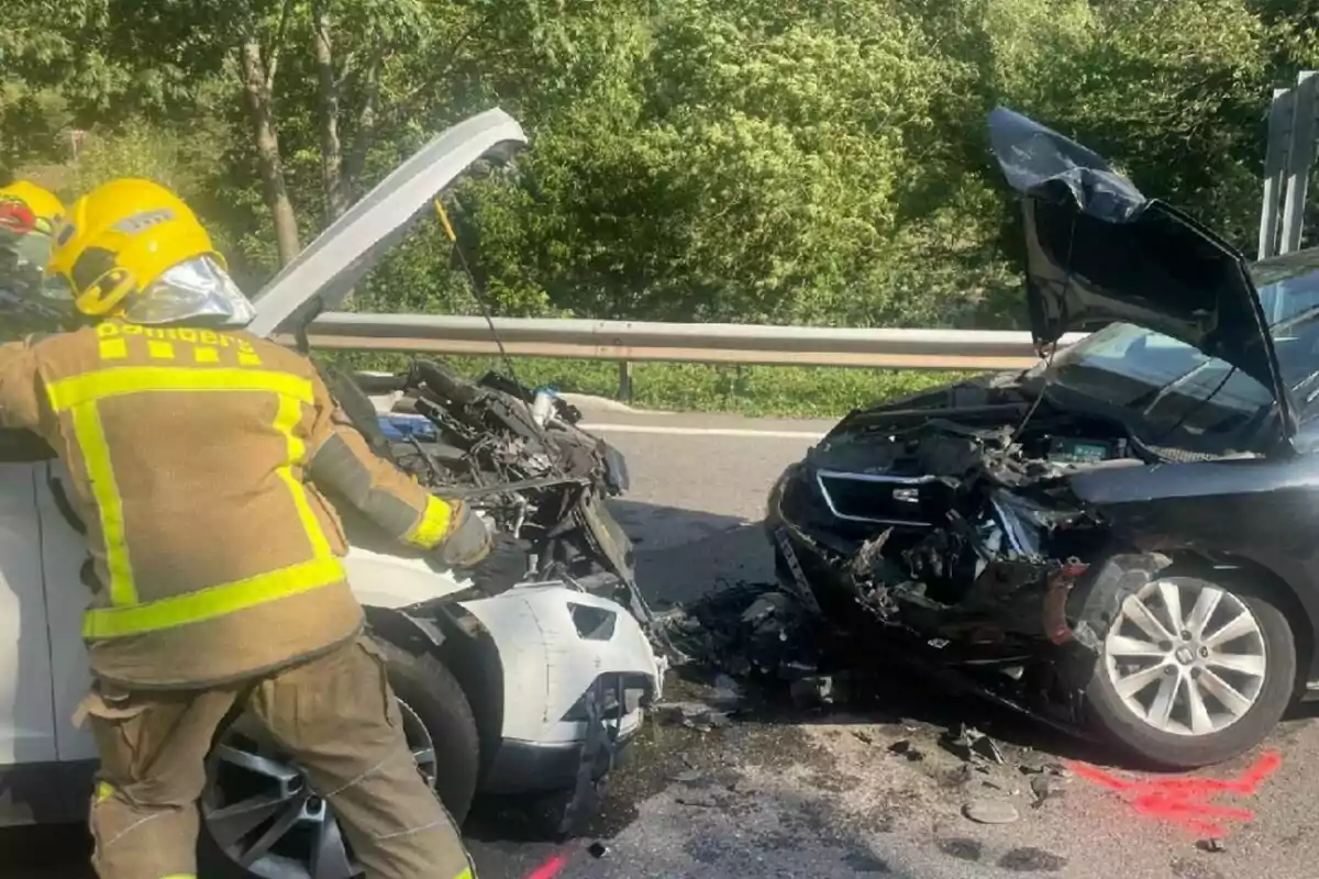 Dos autos chocados de frente en una carretera con un bombero revisando uno de los vehículos y ambos cofres levantados