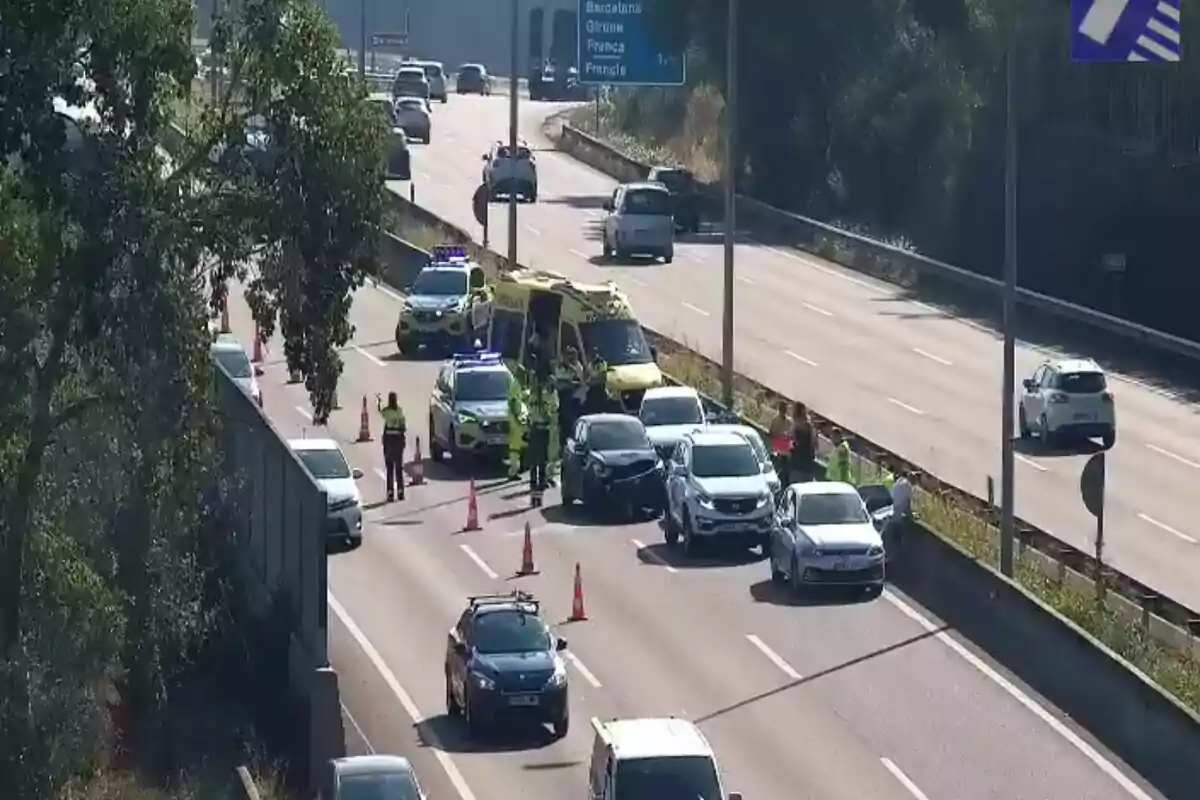 Diversos cotxes i una ambulància aturats en una autopista amb presència de policies i cons de color taronja assenyalant un accident de trànsit.