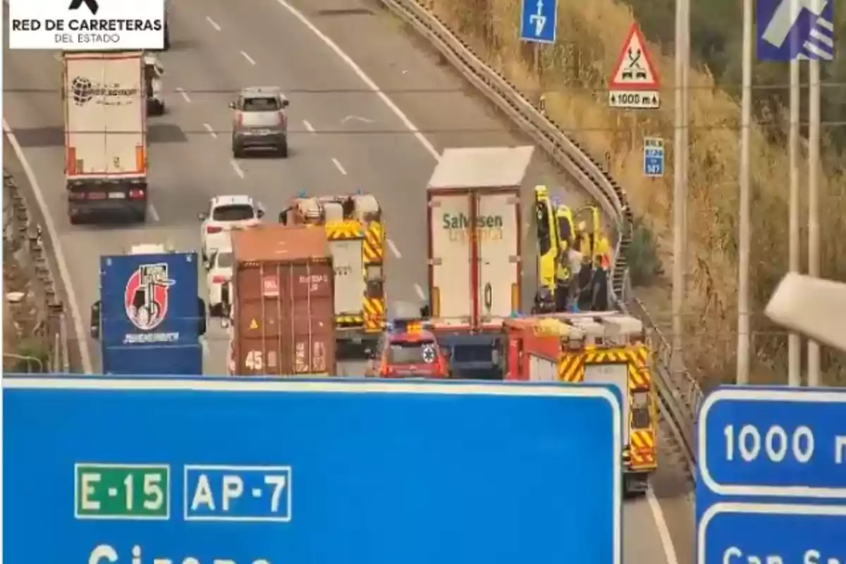Varios vehículos de emergencia y camiones detenidos en una autopista junto a señales de tráfico y un gran cartel azul en primer plano