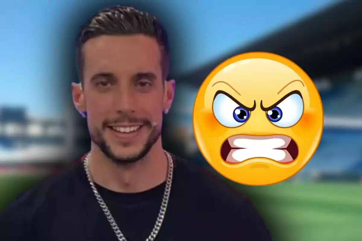 Home somrient amb una cadena platejada i un emoji de cara enfadada al fons en un escenari d’estadi desenfocat