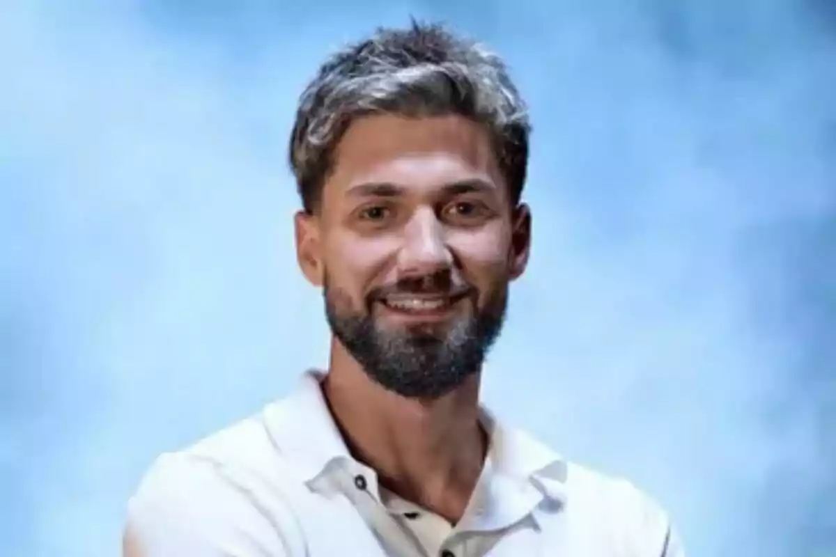 Alejandro Albalá jove amb barba i cabell curt somriu mentre porta una camisa blanca sobre un fons blau difuminat a Supervivientes Alejandro Albalá jove amb barba i cabell curt somriu mentre porta una camisa blanca sobre un fons blau difuminat a Supervivientes