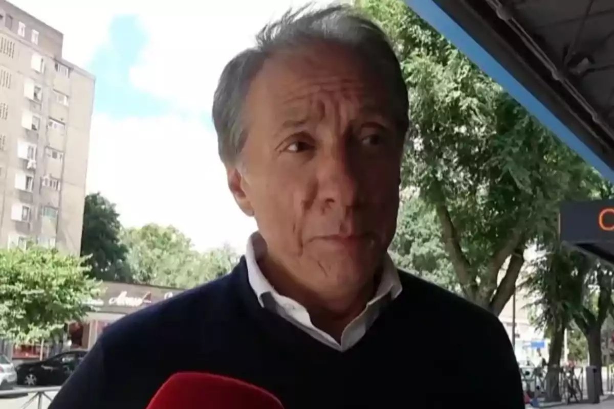 Alejandro Rubio de cabello canoso con suéter oscuro y camisa blanca siendo entrevistado al aire libre en una zona urbana con árboles y edificios al fondo Alejandro Rubio de cabello canoso con suéter oscuro y camisa blanca siendo entrevistado al aire libre en una zona urbana con árboles y edificios al fondo