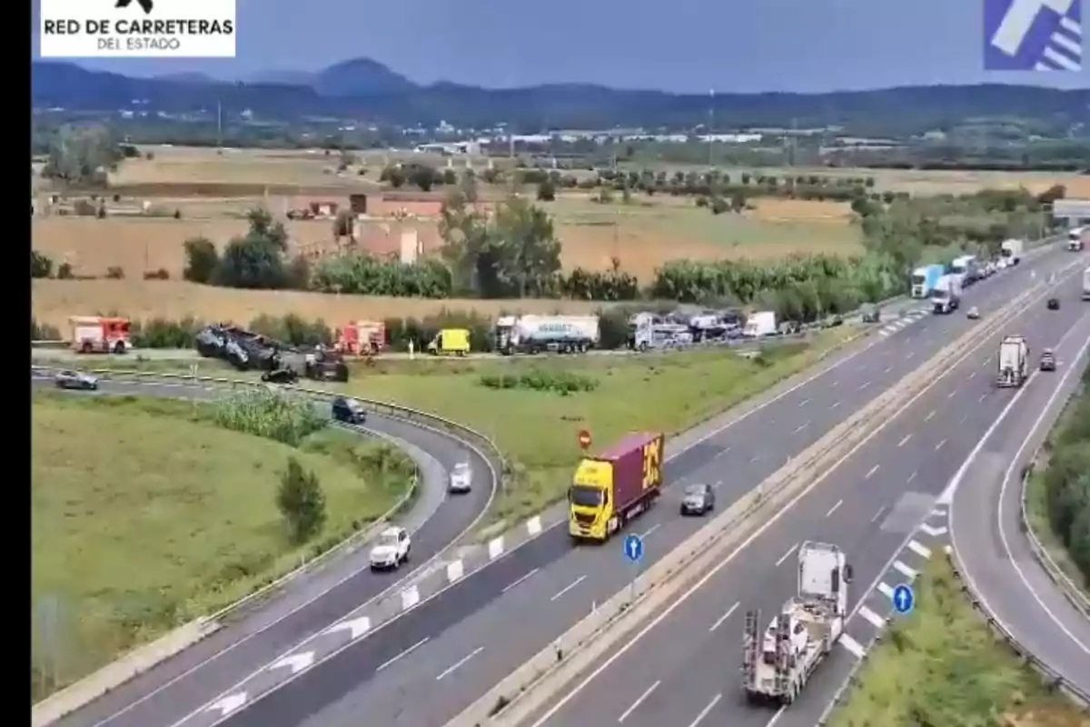 Accidente de tráfico en una autopista con varios camiones y coches detenidos, presencia de vehículos de emergencia y tráfico lento en una zona rural
