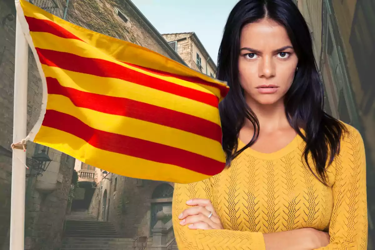 Dona de cabells foscos amb expressió seriosa vestida de groc al costat d’una bandera catalana onejant en un carrer antic
