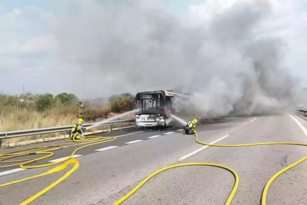 Bomberos apagan el incendio de un autobús en una carretera mientras una gran nube de humo cubre el área
