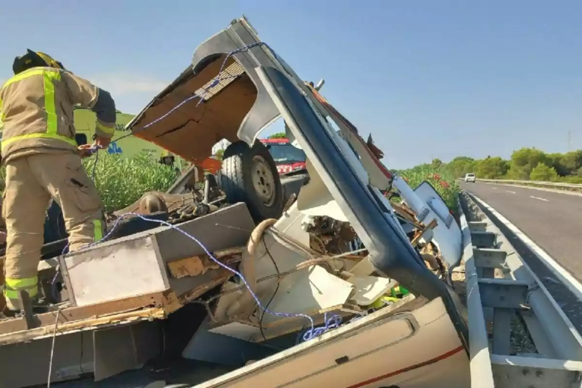 Bombero revisando los restos de una caravana destruida junto a la carretera en un día soleado