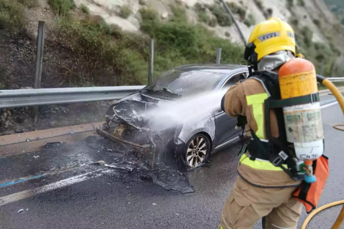 Bombero apaga el incendio en la parte delantera de un automóvil quemado en una carretera