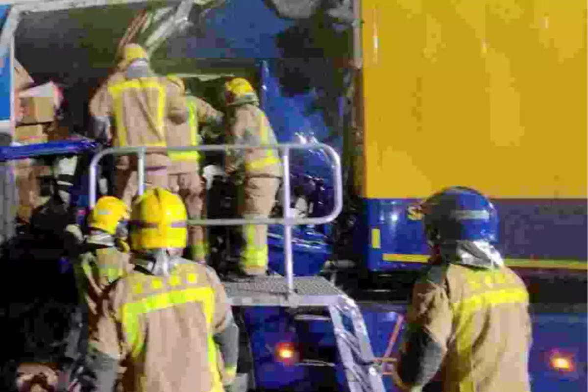 Bombers amb cascos i equip de protecció treballen en el rescat de persones atrapades a la cabina d’un camió després d’un accident viari.