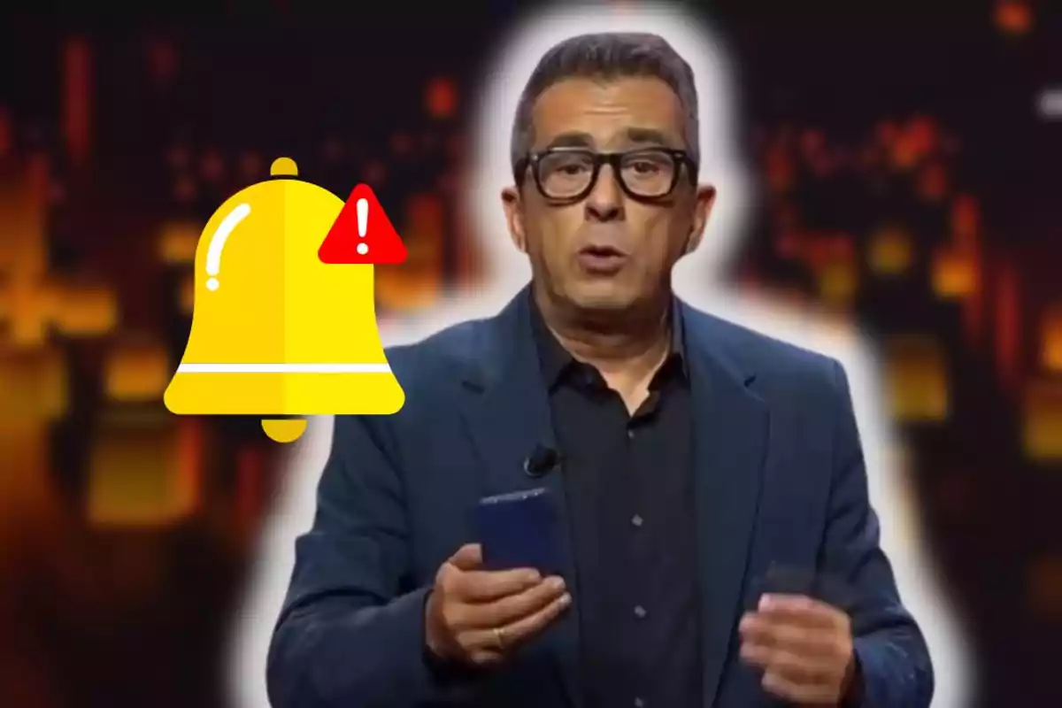 Hombre con gafas y chaqueta oscura sosteniendo un teléfono móvil con un ícono de campana de advertencia amarilla al lado