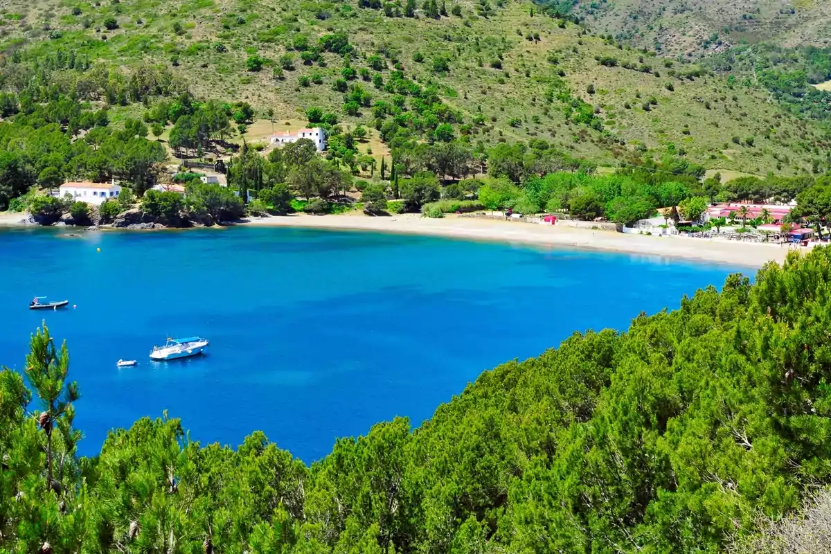 Playa de aguas cristalinas rodeada de colinas verdes con algunas casas y barcos flotando en el mar Playa de aguas cristalinas rodeada de colinas verdes con algunas casas y barcos flotando en el mar