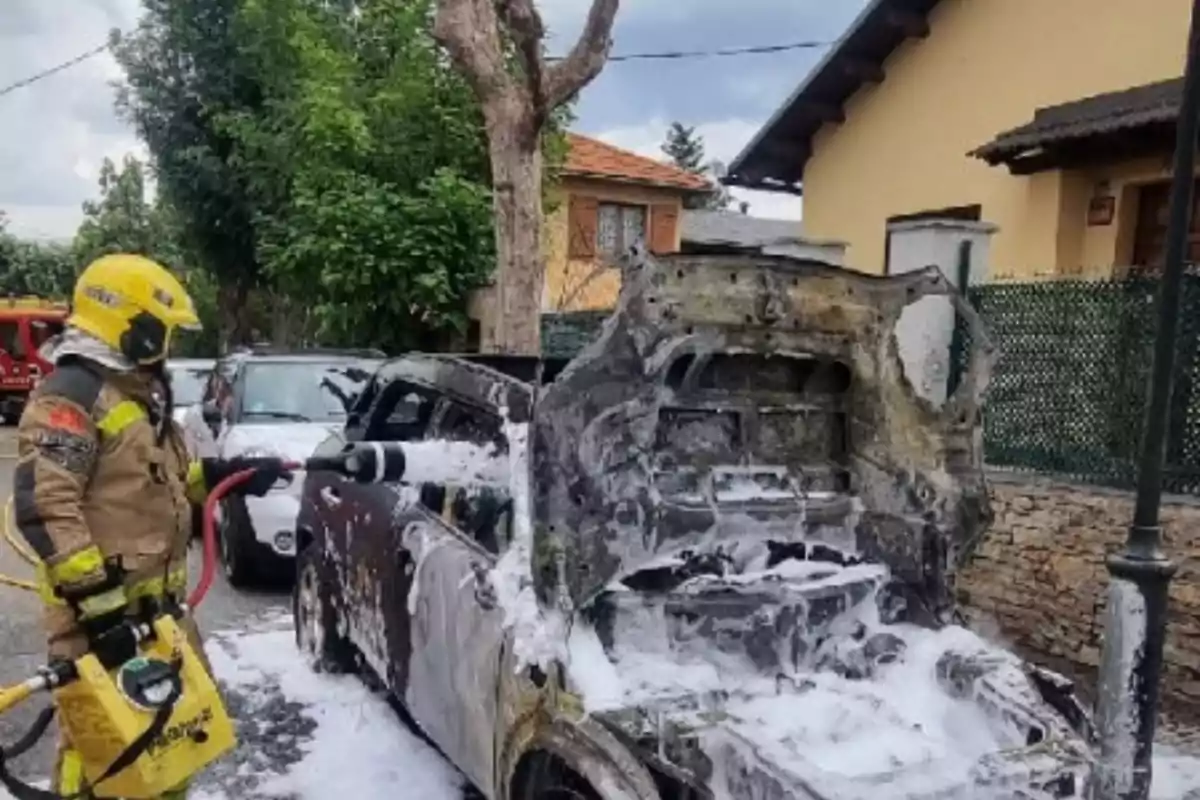 Un bomber apaga un incendi en un cotxe cremat fent servir escuma en un carrer residencial Un bomber apaga un incendi en un cotxe cremat fent servir escuma en un carrer residencial