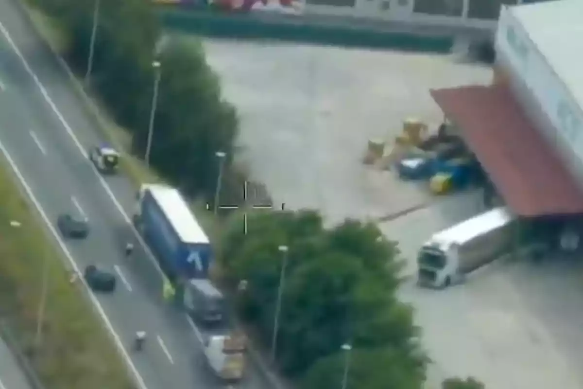 Vista aérea de un camión detenido en una carretera junto a un edificio industrial con varios vehículos alrededor