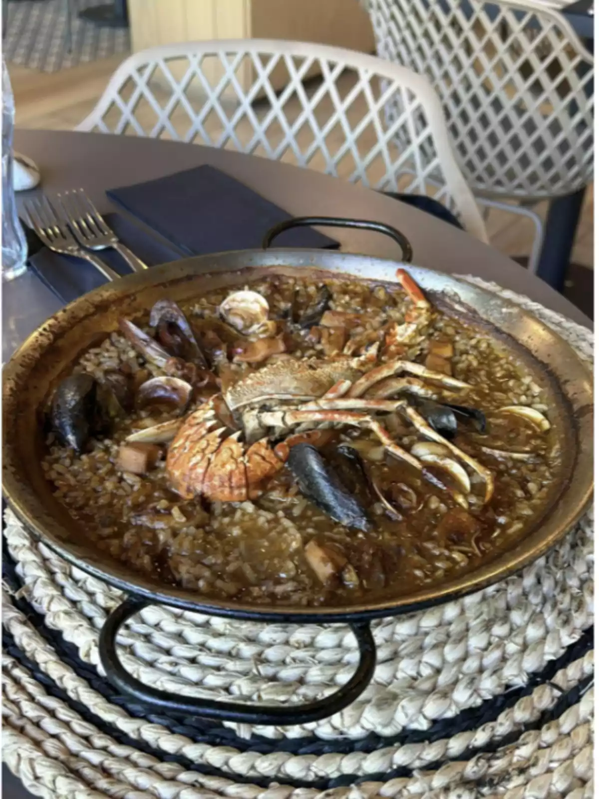 Paella de marisc servida en una taula de restaurant amb coberts i tovalló al fons Paella de marisc servida en una taula de restaurant amb coberts i tovalló al fons