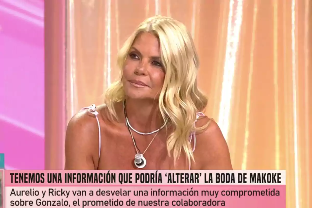 Makoke con vestido claro sentada en un plató de televisión con fondo rosa y texto en pantalla sobre información que podría alterar una boda Makoke con vestido claro sentada en un plató de televisión con fondo rosa y texto en pantalla sobre información que podría alterar una boda