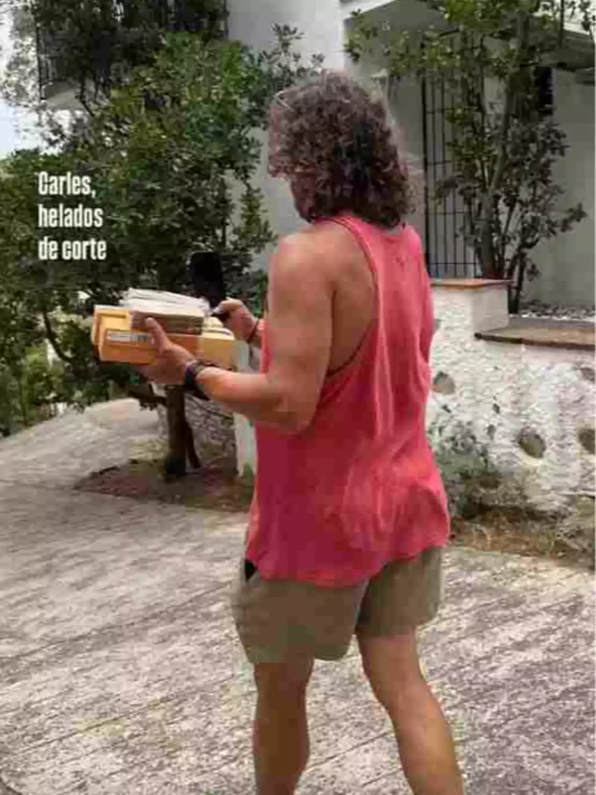 Home d’esquena amb samarreta de tirants vermella i pantalons curts beix caminant per un camí mentre sosté diversos gelats i un telèfon mòbil Home d’esquena amb samarreta de tirants vermella i pantalons curts beix caminant per un camí mentre sosté diversos gelats i un telèfon mòbil