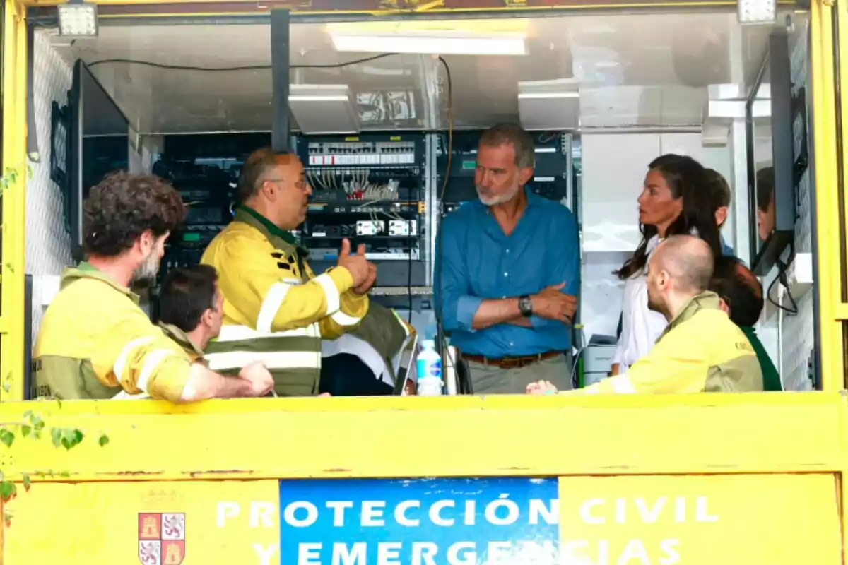 Varias personas conversan dentro de una unidad móvil de protección civil y emergencias, algunas llevan uniformes amarillos y otras ropa de calle, rodeados de equipos electrónicos. Varias personas conversan dentro de una unidad móvil de protección civil y emergencias, algunas llevan uniformes amarillos y otras ropa de calle, rodeados de equipos electrónicos.