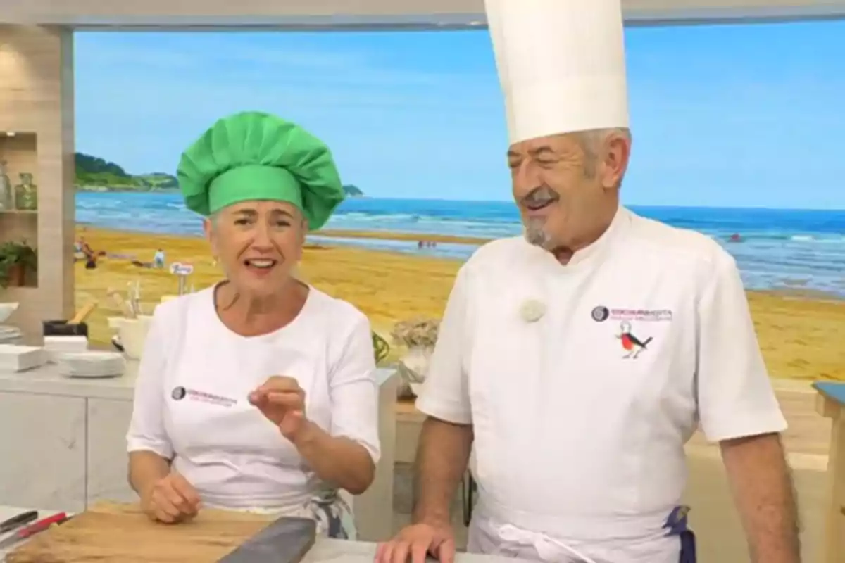 Eva i Karlos Arguiñano somrients amb barrets de cuina, un de verd i l’altre de blanc, són en una cuina amb un fons de platja. Captura de ‘Cocina Abierta’ Eva i Karlos Arguiñano somrients amb barrets de cuina, un de verd i l’altre de blanc, són en una cuina amb un fons de platja. Captura de ‘Cocina Abierta’