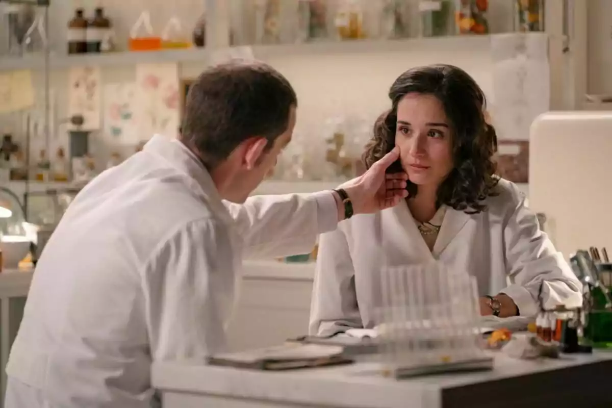Un home, que és Guillermo Barrientos, toca la galta d’una dona, que és Sara Sanz, que sembla estar trista mentre tots dos porten bates de laboratori i es troben en un entorn científic. Un home, que és Guillermo Barrientos, toca la galta d’una dona, que és Sara Sanz, que sembla estar trista mentre tots dos porten bates de laboratori i es troben en un entorn científic.