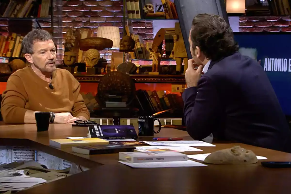 Antonio Banderas i Iker Jiménez conversen en un estudi de televisió decorat amb llibres i objectes antics mentre estan asseguts en una taula amb tasses, llibres i papers. Captura de 'Cuarto Milenio' Antonio Banderas i Iker Jiménez conversen en un estudi de televisió decorat amb llibres i objectes antics mentre estan asseguts en una taula amb tasses, llibres i papers. Captura de 'Cuarto Milenio'
