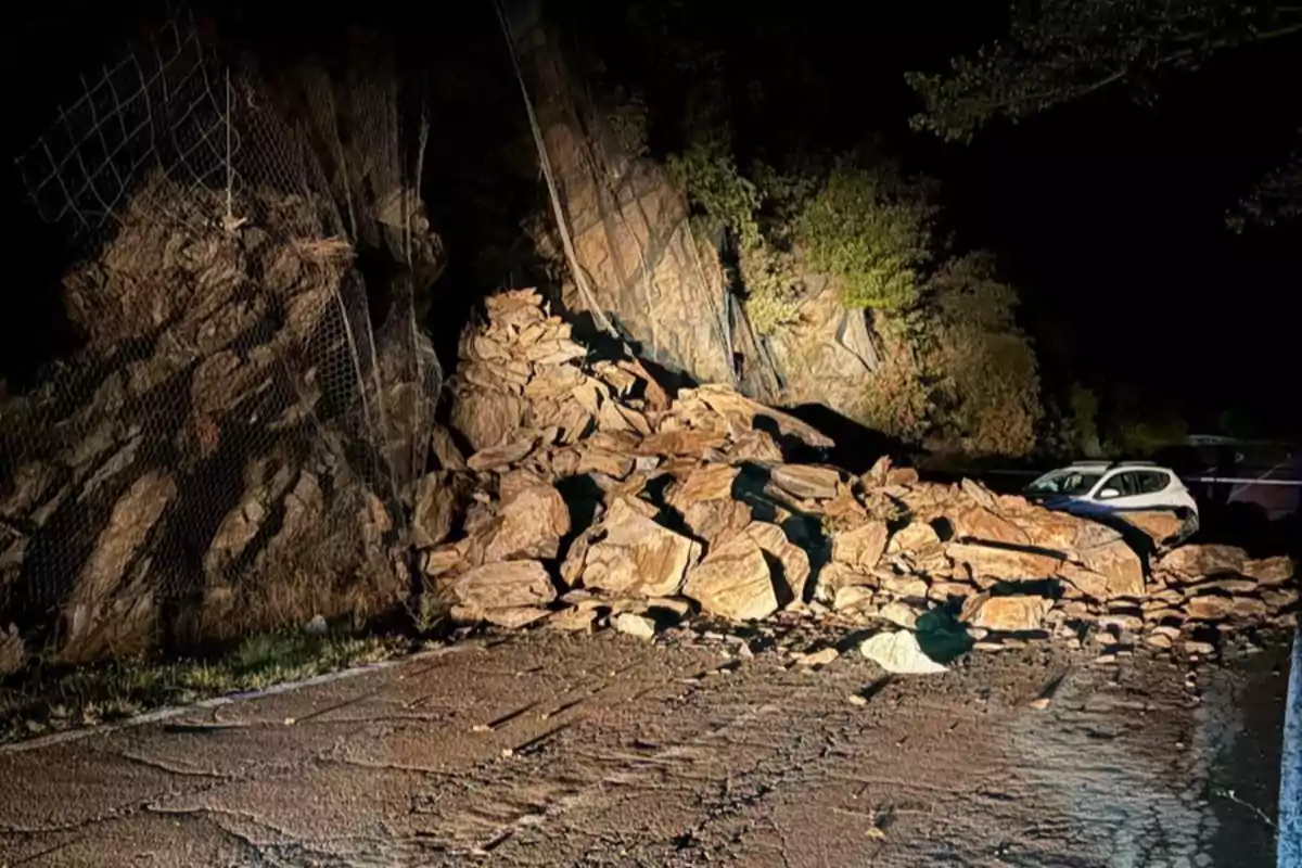 Un derrumbe de rocas bloquea una carretera durante la noche y un coche blanco queda atrapado entre las piedras.