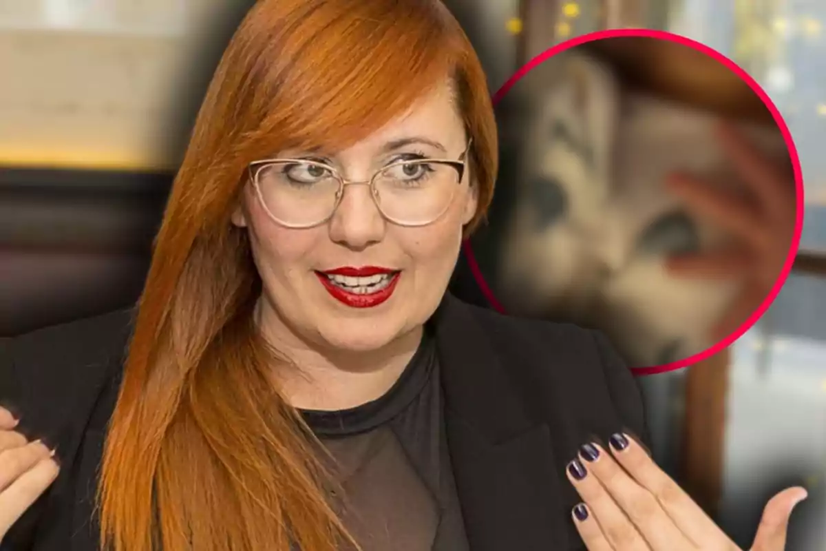Mujer pelirroja con gafas y labios rojos hablando, lleva una chaqueta negra y al fondo hay un círculo con una imagen borrosa de una máscara.