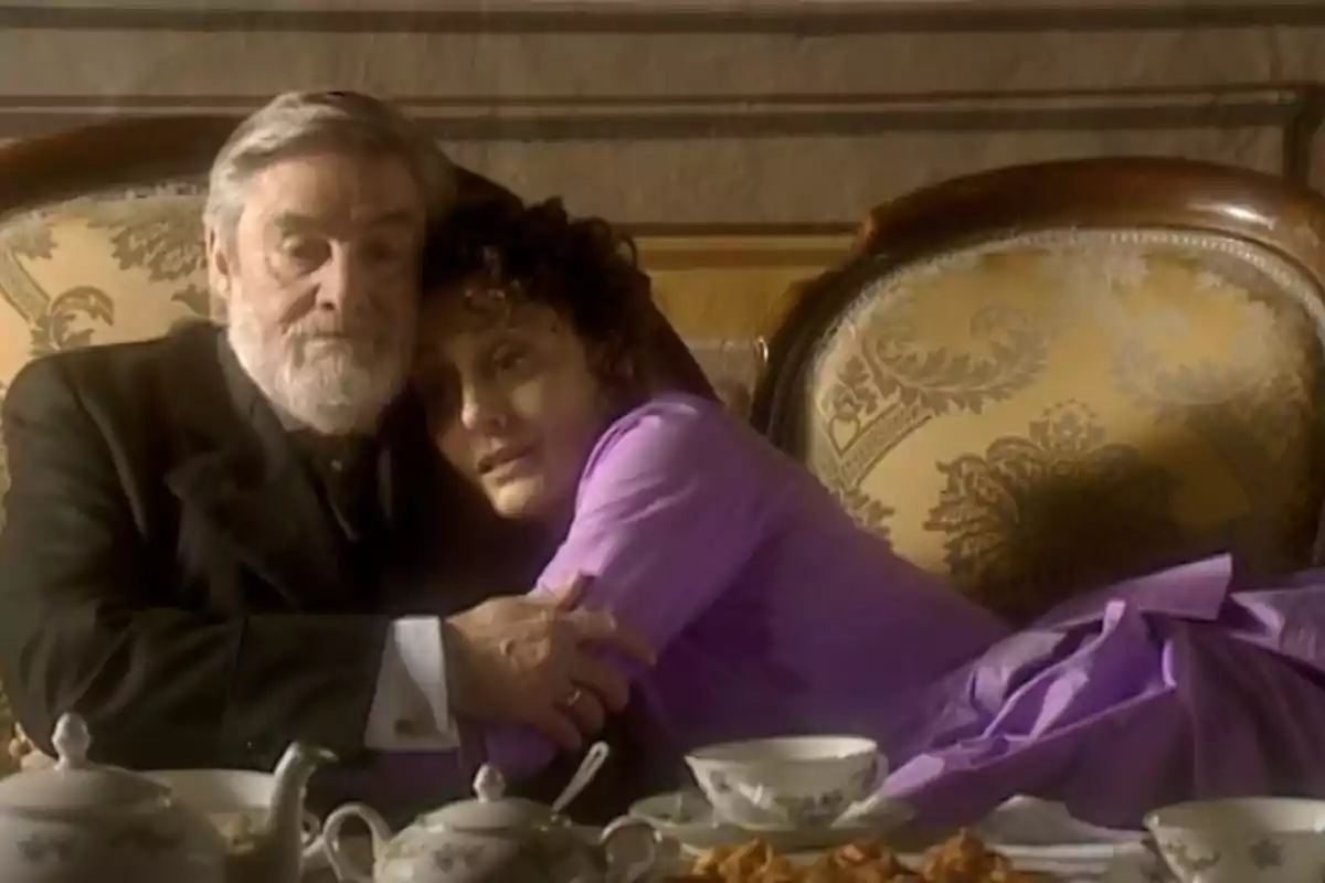 Parella de persones grans assegudes en un sofà elegant abraçant-se amb una taula de te al davant Parella de persones grans assegudes en un sofà elegant abraçant-se amb una taula de te al davant
