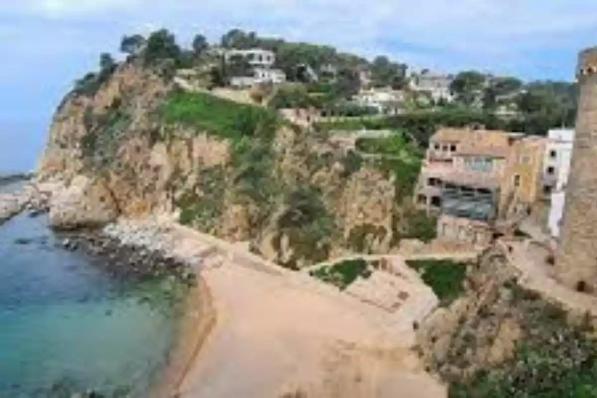 Vista de un acantilado con casas y vegetación junto a una playa de arena y mar azul Vista de un acantilado con casas y vegetación junto a una playa de arena y mar azul