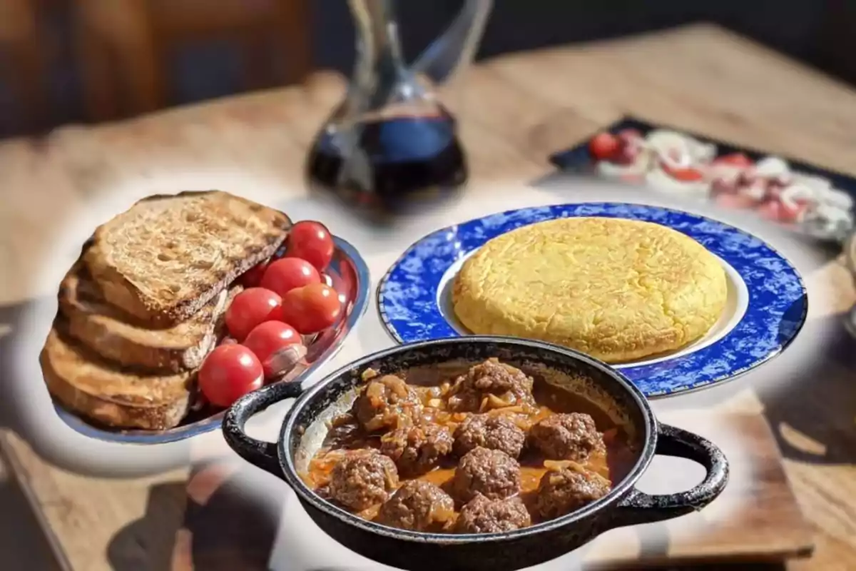 Plat d’albóndigues amb salsa acompanyat d’una truita de patates, llesques de pa torrat i tomàquets cherry sobre una taula de fusta