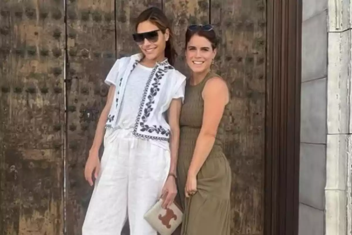Ayda Field Williams and Eugenie of York pose smiling in front of an old wooden door. Ayda Field Williams and Eugenie of York pose smiling in front of an old wooden door.