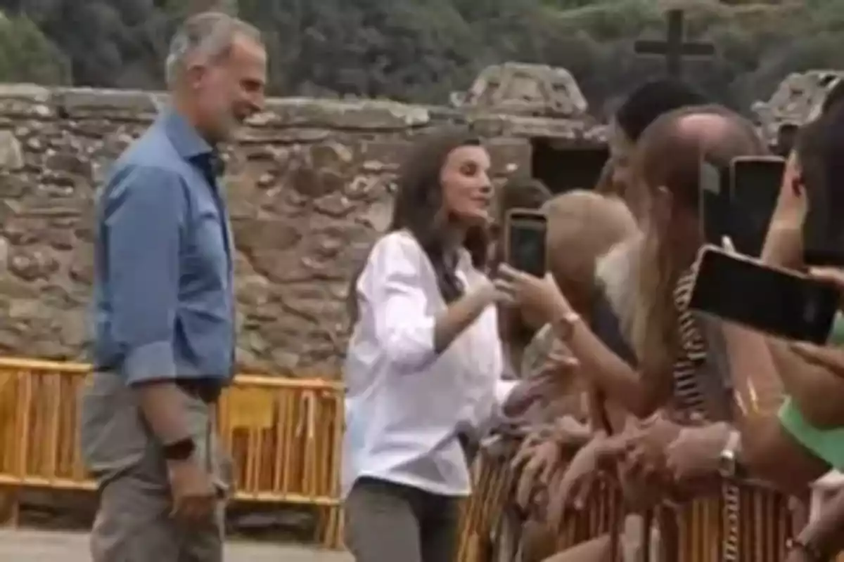 Felipe VI y la reina Letizia saluda y conversa con un grupo de personas que los fotografían con sus teléfonos móviles frente a una pared de piedra al aire libre. Felipe VI y la reina Letizia saluda y conversa con un grupo de personas que los fotografían con sus teléfonos móviles frente a una pared de piedra al aire libre.