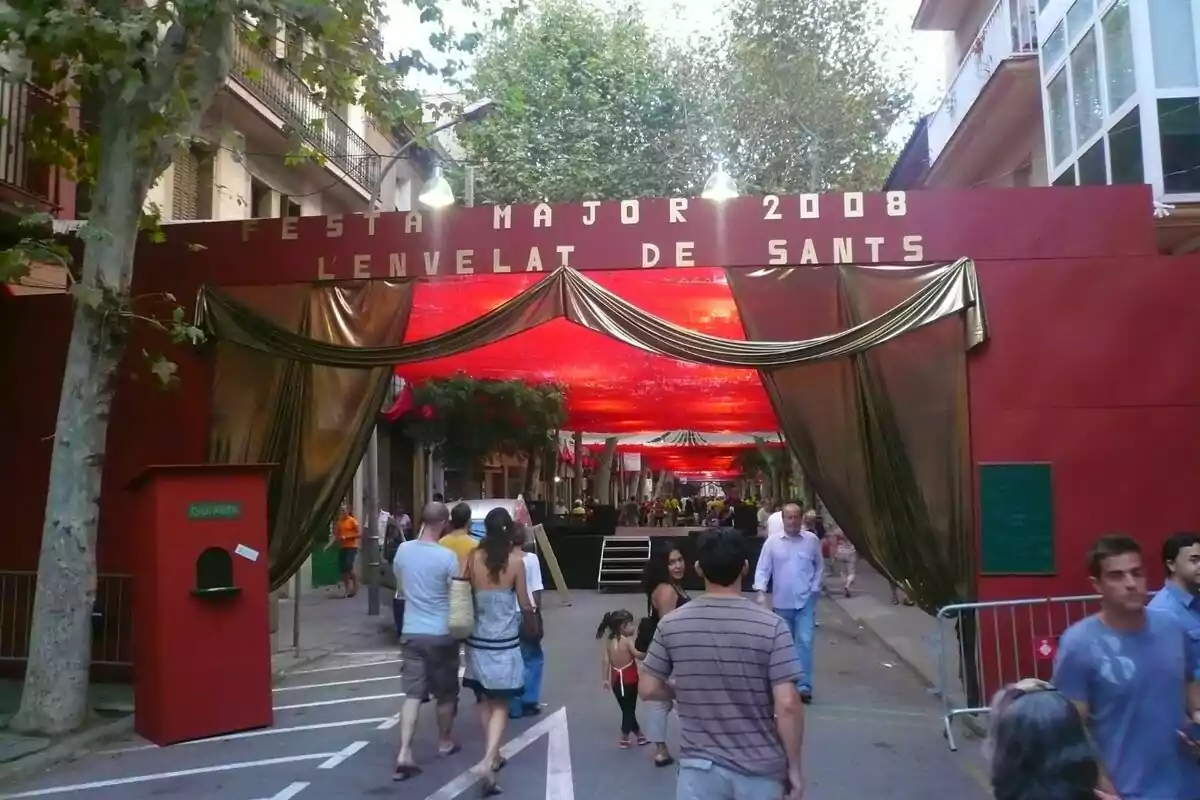 Entrada decorada d’un carrer durant la Festa Major de Sants 2008 amb persones caminant sota tendals vermells i daurats Entrada decorada d’un carrer durant la Festa Major de Sants 2008 amb persones caminant sota tendals vermells i daurats