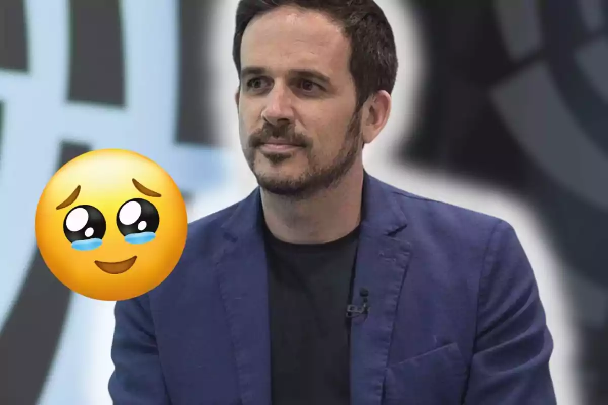 Home amb jaqueta blava i samarreta negra assegut davant d’un fons desenfocat amb un emoji de carona tendra i ulls plorosos al seu costat