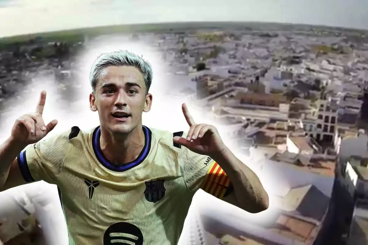 Un futbolista amb uniforme daurat celebra aixecant tots dos braços davant d’una imatge difuminada d’una ciutat vista des de dalt.