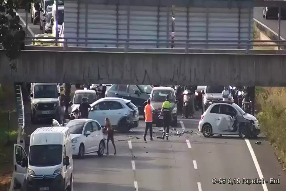 Varios autos chocados y personas en la carretera bajo un puente, con tráfico detenido y escombros en el asfalto