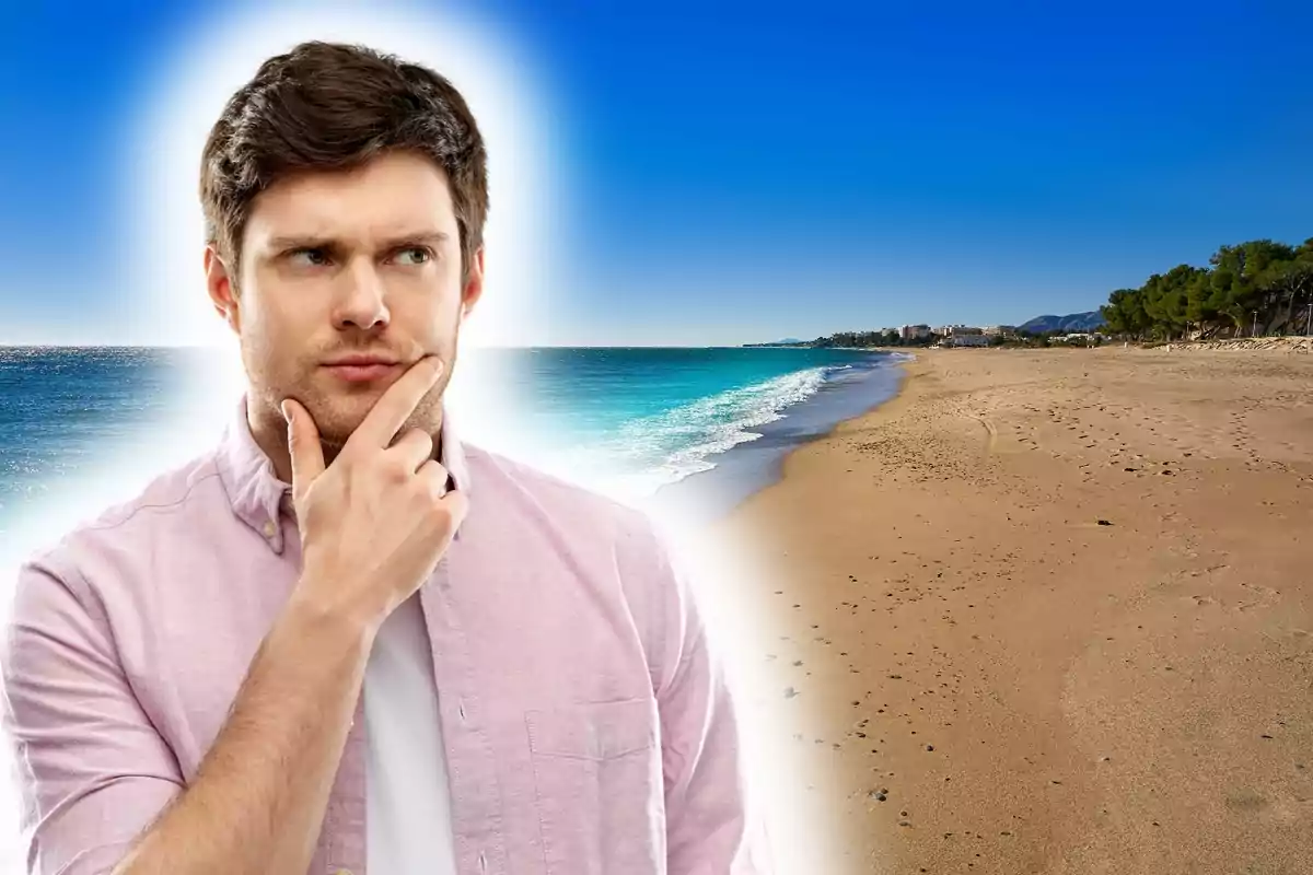 Home pensatiu amb camisa rosa davant d’una platja de sorra i mar blau sota un cel serè