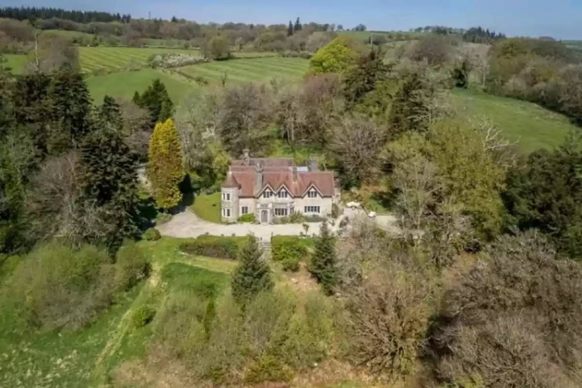Vista aèria d’una casa gran d’estil clàssic envoltada d’arbres i vegetació en un entorn rural Vista aèria d’una casa gran d’estil clàssic envoltada d’arbres i vegetació en un entorn rural