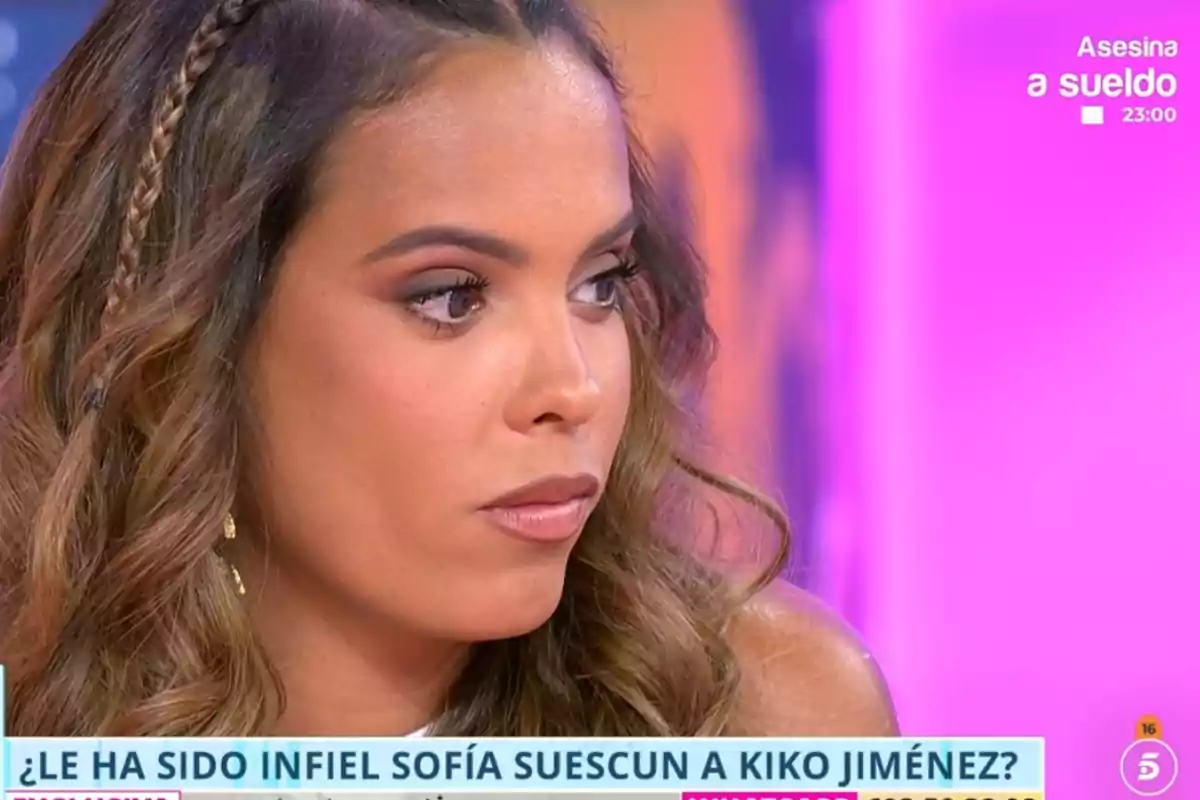 Gloria Camila con expresión seria en un programa de televisión con fondo rosa y texto en pantalla sobre una posible infidelidad