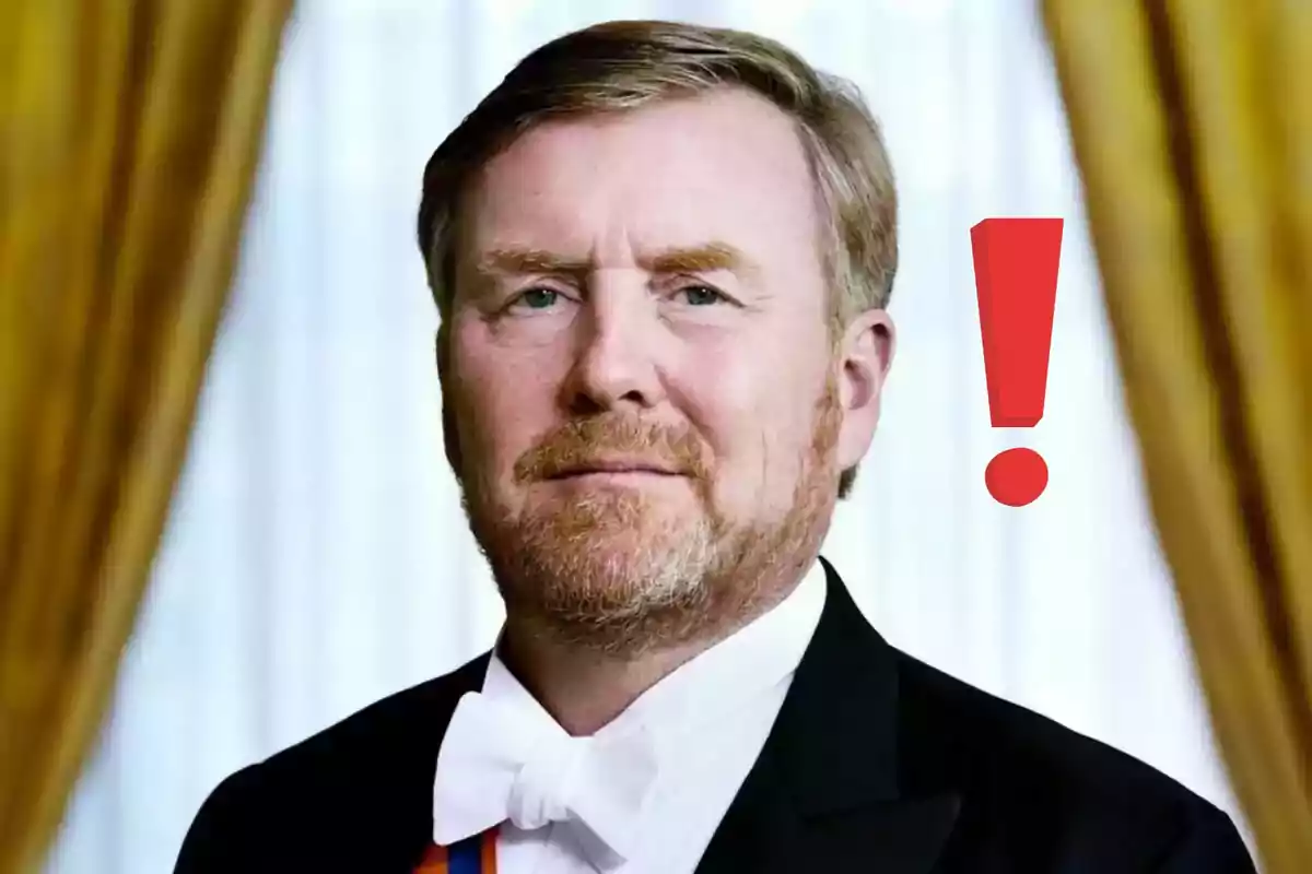 Guillermo de Holanda de barba rubia con esmoquin y moño blanco, al fondo cortinas doradas y un signo de exclamación rojo a su lado