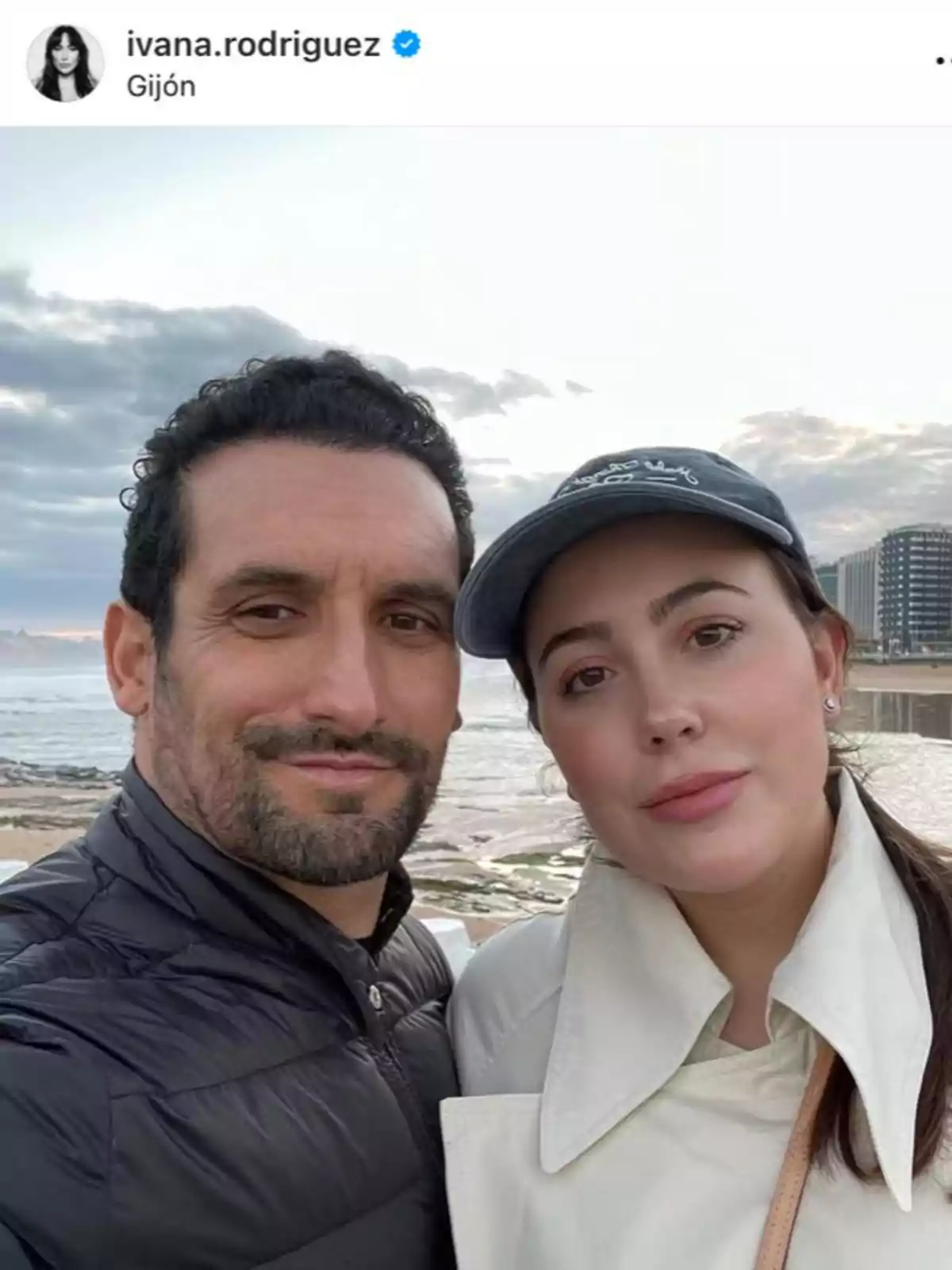 Ivana Rodríguez y su marido tomándose una selfie en la playa con edificios y el mar de fondo en un día nublado Ivana Rodríguez y su marido tomándose una selfie en la playa con edificios y el mar de fondo en un día nublado
