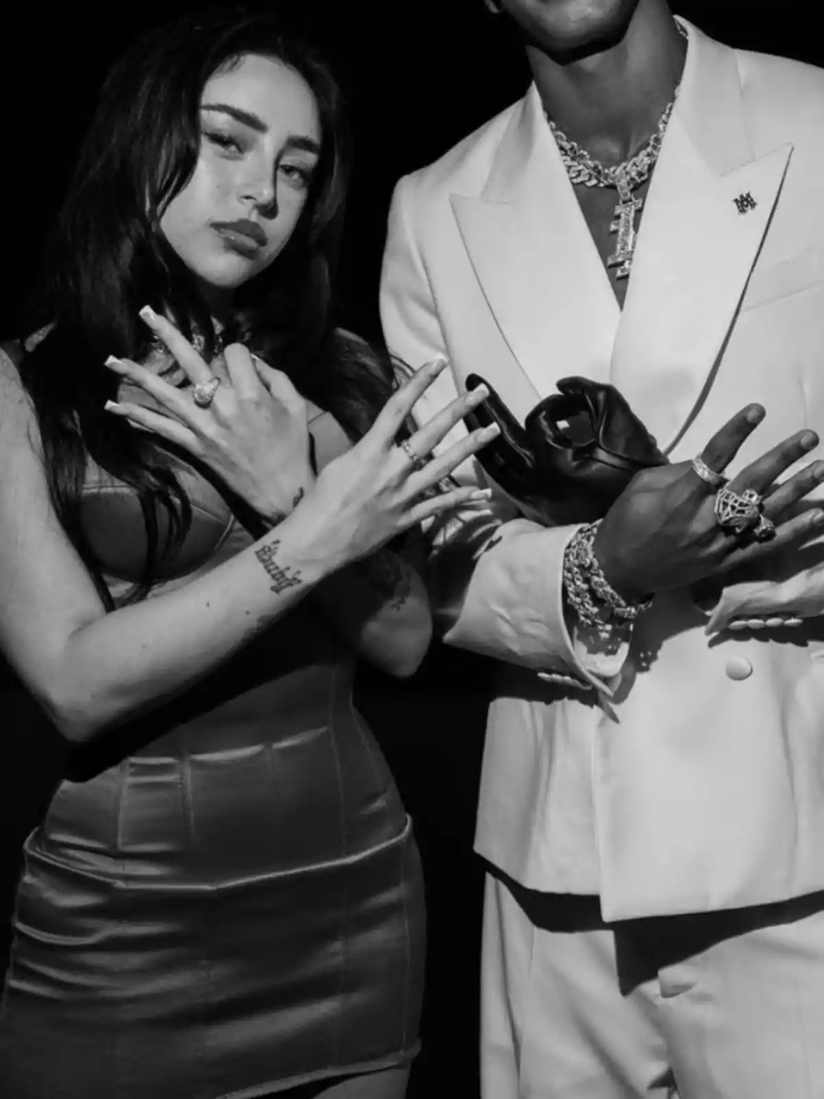 Two people pose in black and white, showing their hands with rings and gestures; one wears a fitted dress and the other an elegant suit with chains and gloves. Two people pose in black and white, showing their hands with rings and gestures; one wears a fitted dress and the other an elegant suit with chains and gloves.