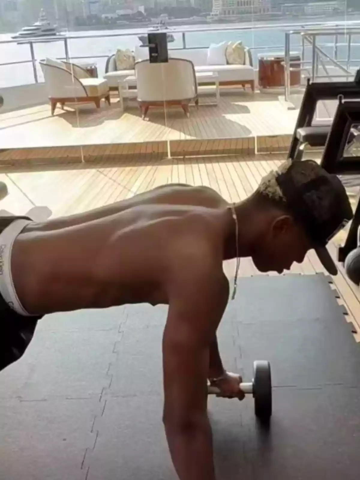 Shirtless young man working out with dumbbells on the deck of a yacht overlooking the sea, with outdoor furniture in the background Shirtless young man working out with dumbbells on the deck of a yacht overlooking the sea, with outdoor furniture in the background