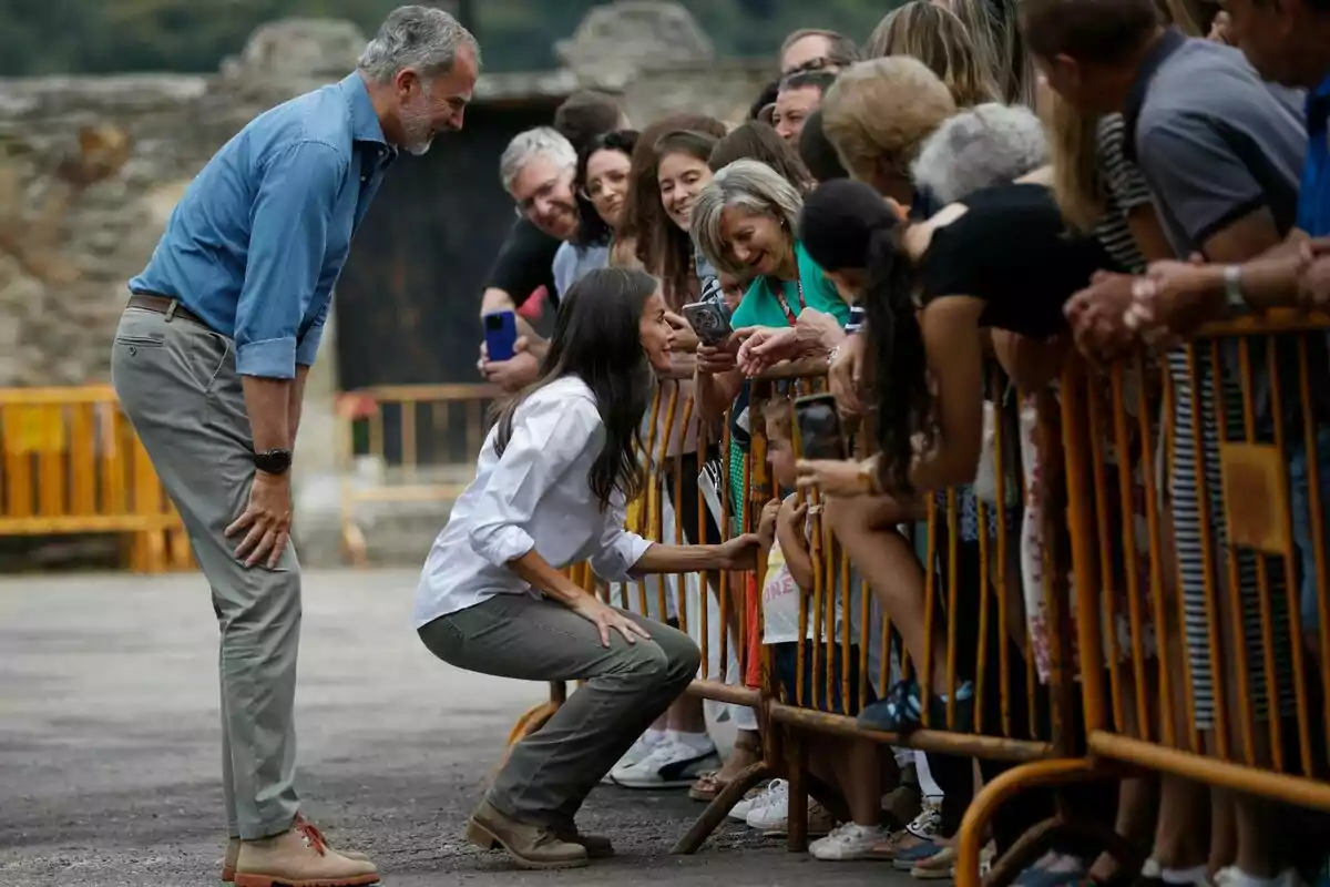 A man and a woman greet and talk with a group of people behind a fence in an outdoor setting. A man and a woman greet and talk with a group of people behind a fence in an outdoor setting.