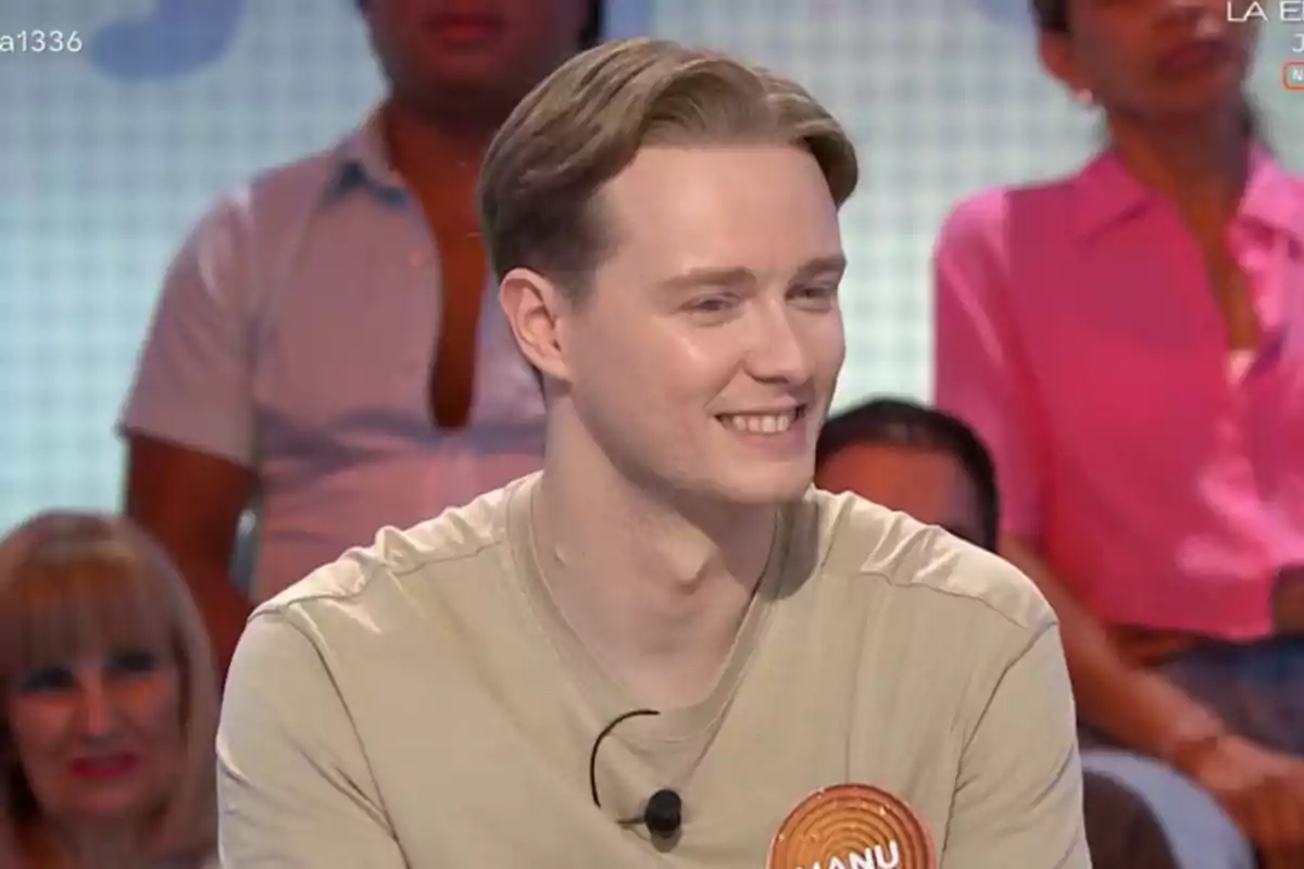 Un jove de cabells rossos somriu mentre participa en un programa de televisió amb públic al fons. Un jove de cabells rossos somriu mentre participa en un programa de televisió amb públic al fons.