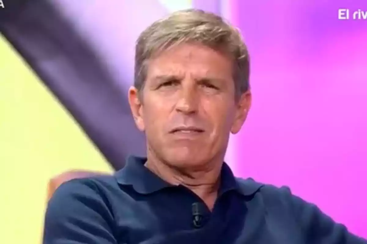 Manuel ‘El Cordobés’ de cabello corto y rubio con expresión seria vistiendo una camiseta tipo polo azul en un set de televisión con fondo colorido Manuel ‘El Cordobés’ de cabello corto y rubio con expresión seria vistiendo una camiseta tipo polo azul en un set de televisión con fondo colorido