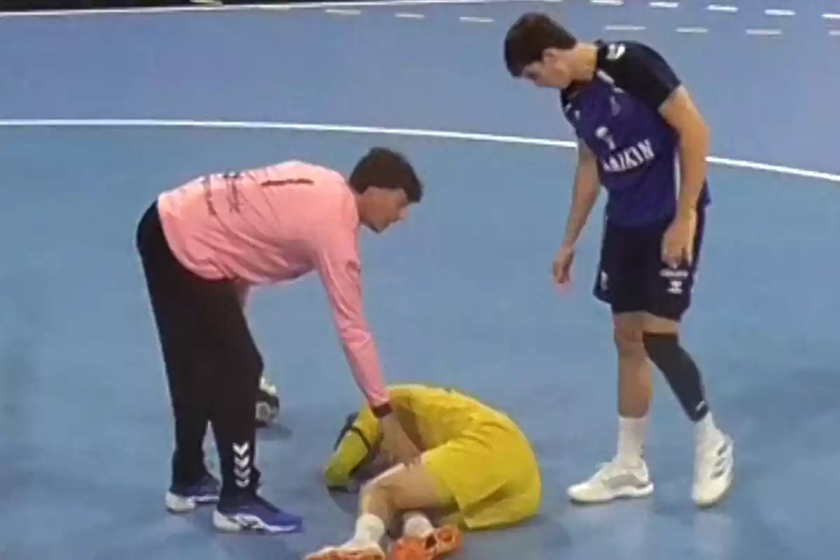 Un jugador d’handbol està estirat a terra mentre dos companys l’assisteixen a la pista. Un jugador d’handbol està estirat a terra mentre dos companys l’assisteixen a la pista.