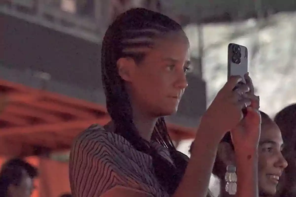 Young person with braids recording a video with their phone at an indoor event Young person with braids recording a video with their phone at an indoor event