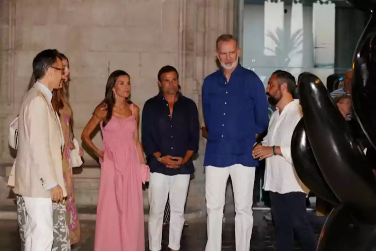 Un grupo de personas elegantemente vestidas conversa en el interior de un edificio junto a una escultura negra Un grupo de personas elegantemente vestidas conversa en el interior de un edificio junto a una escultura negra